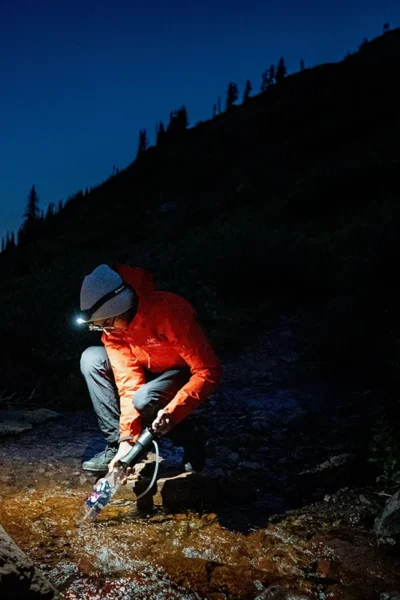 Persoon die water filtert met een draagbaar waterfilter in een noodsituatie in de buitenlucht
