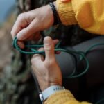 Handen die een knoop leggen in een groen paracord touw