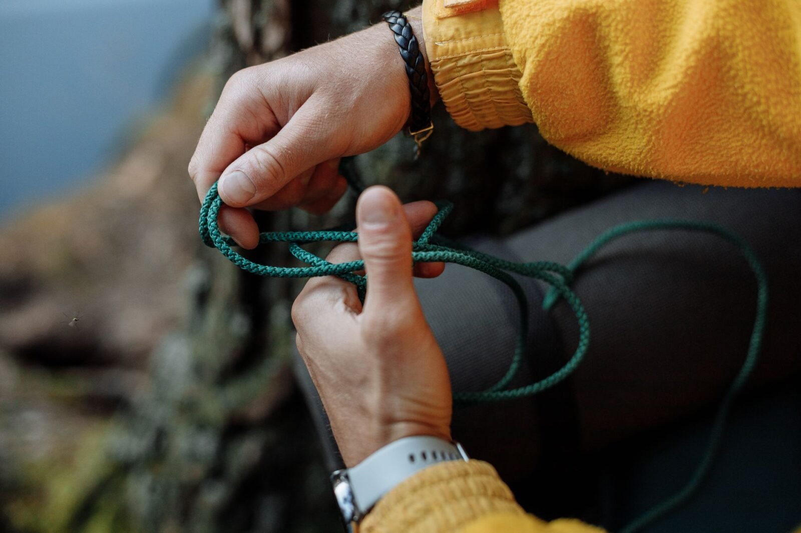 Handen die een knoop leggen in een groen paracord touw