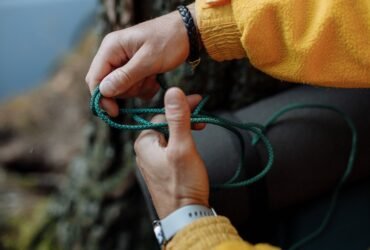 Handen die een knoop leggen in een groen paracord touw