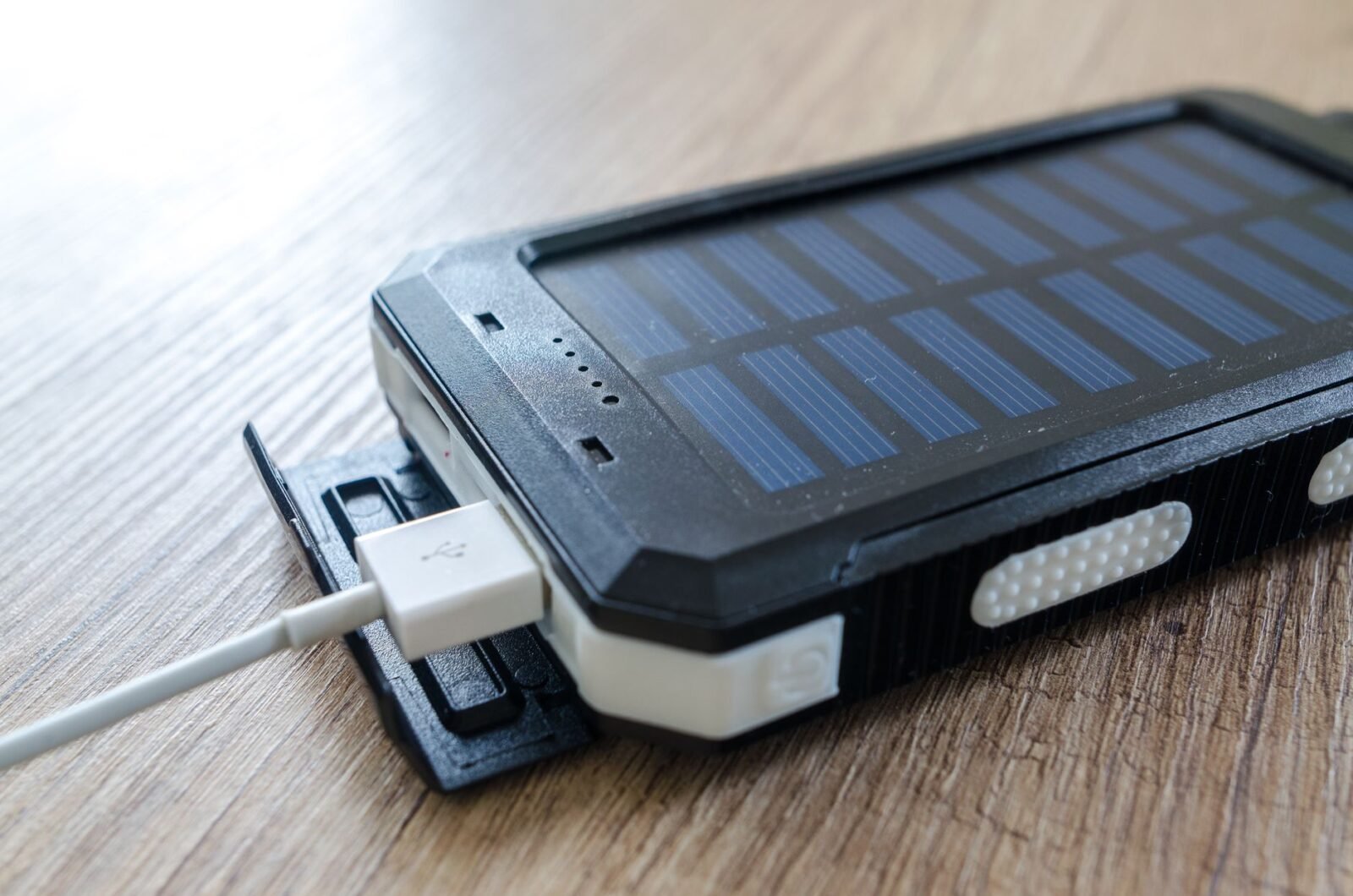 Powerbank met zonnepaneel en een aangesloten USB-kabel op een houten tafel
