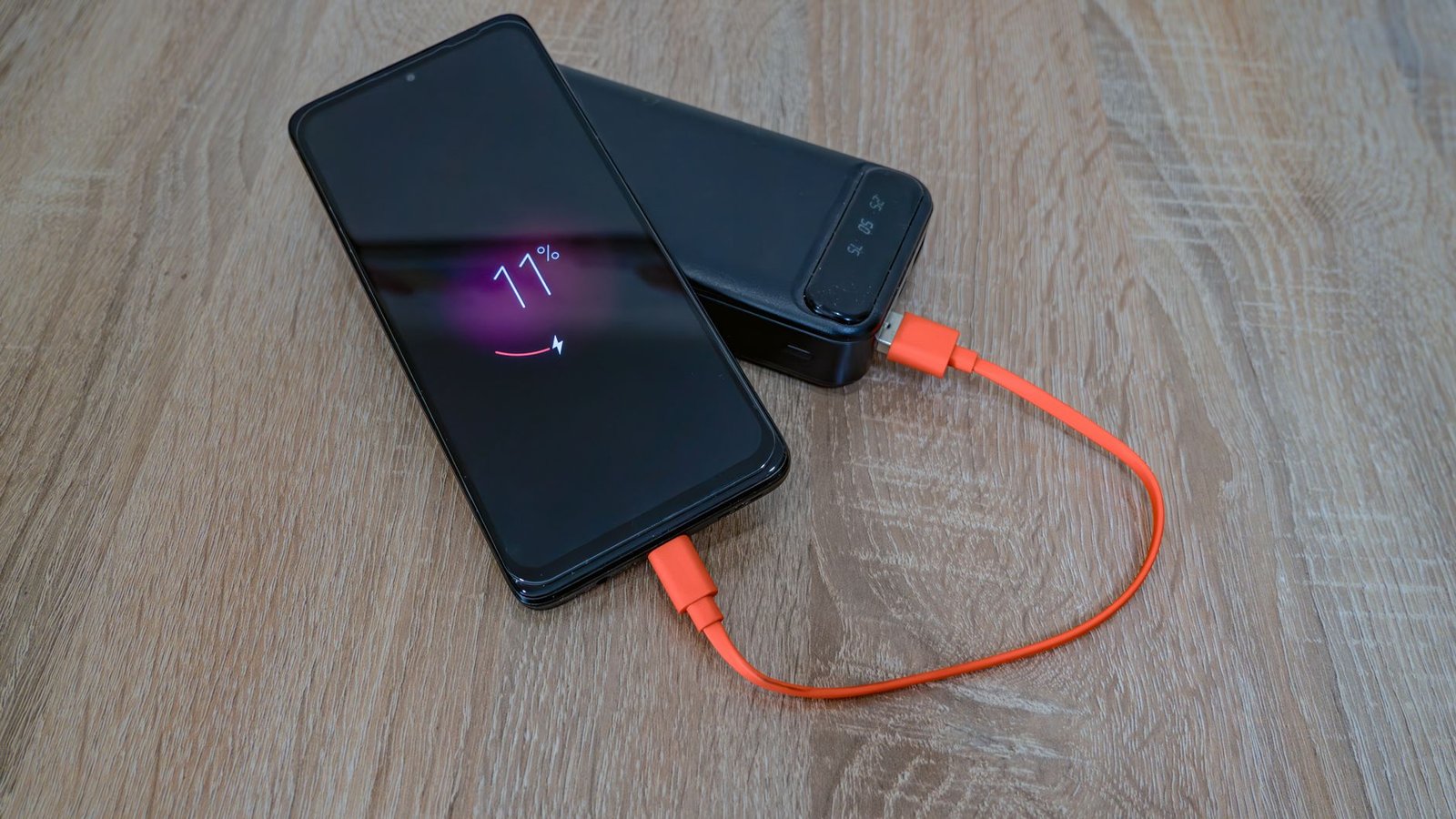 Smartphone die oplaadt via een powerbank met een oranje kabel