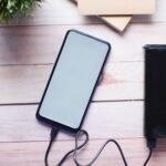 Smartphone wordt opgeladen met een zwarte powerbank op een houten tafel