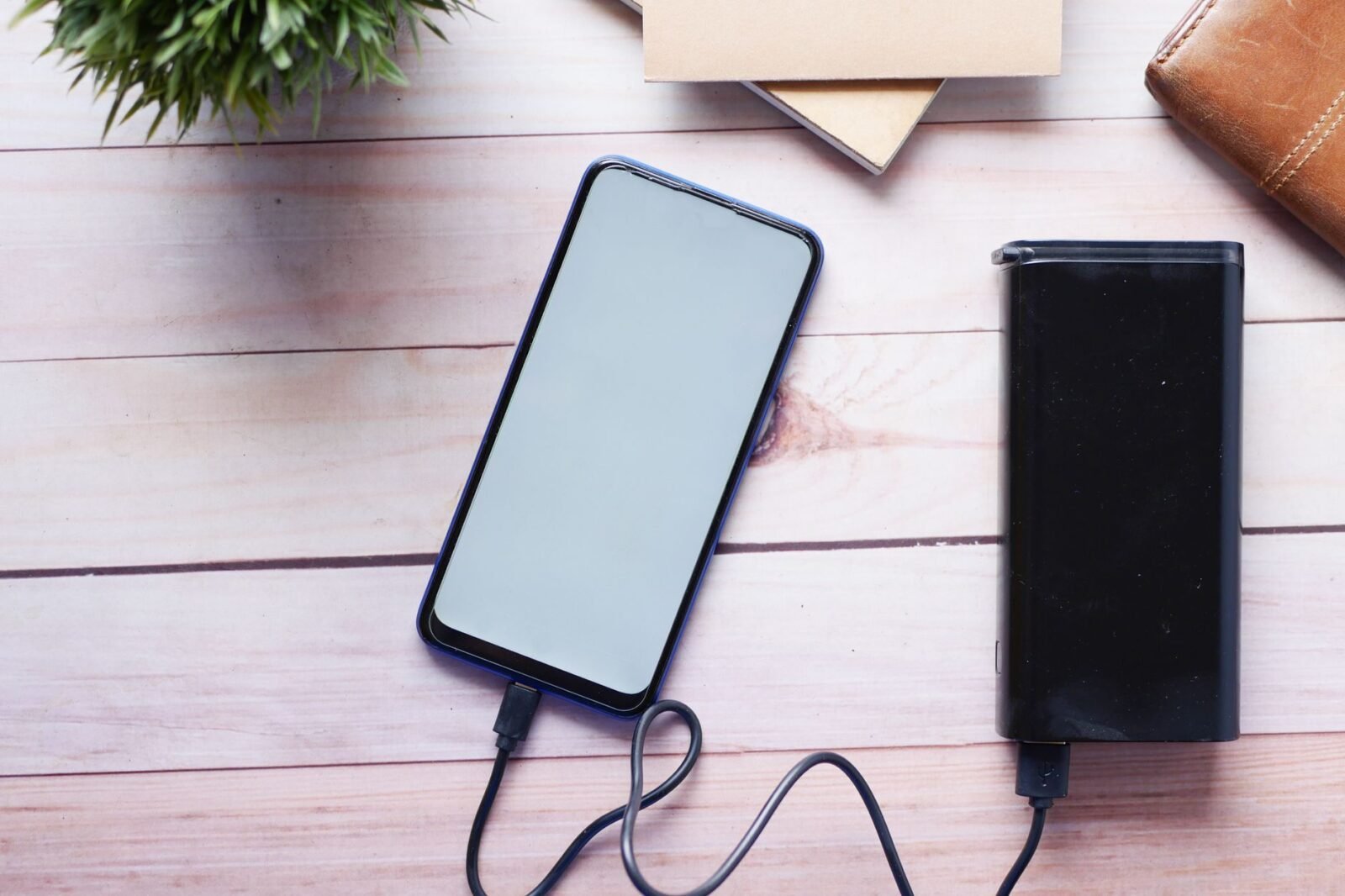 Smartphone wordt opgeladen met een zwarte powerbank op een houten tafel