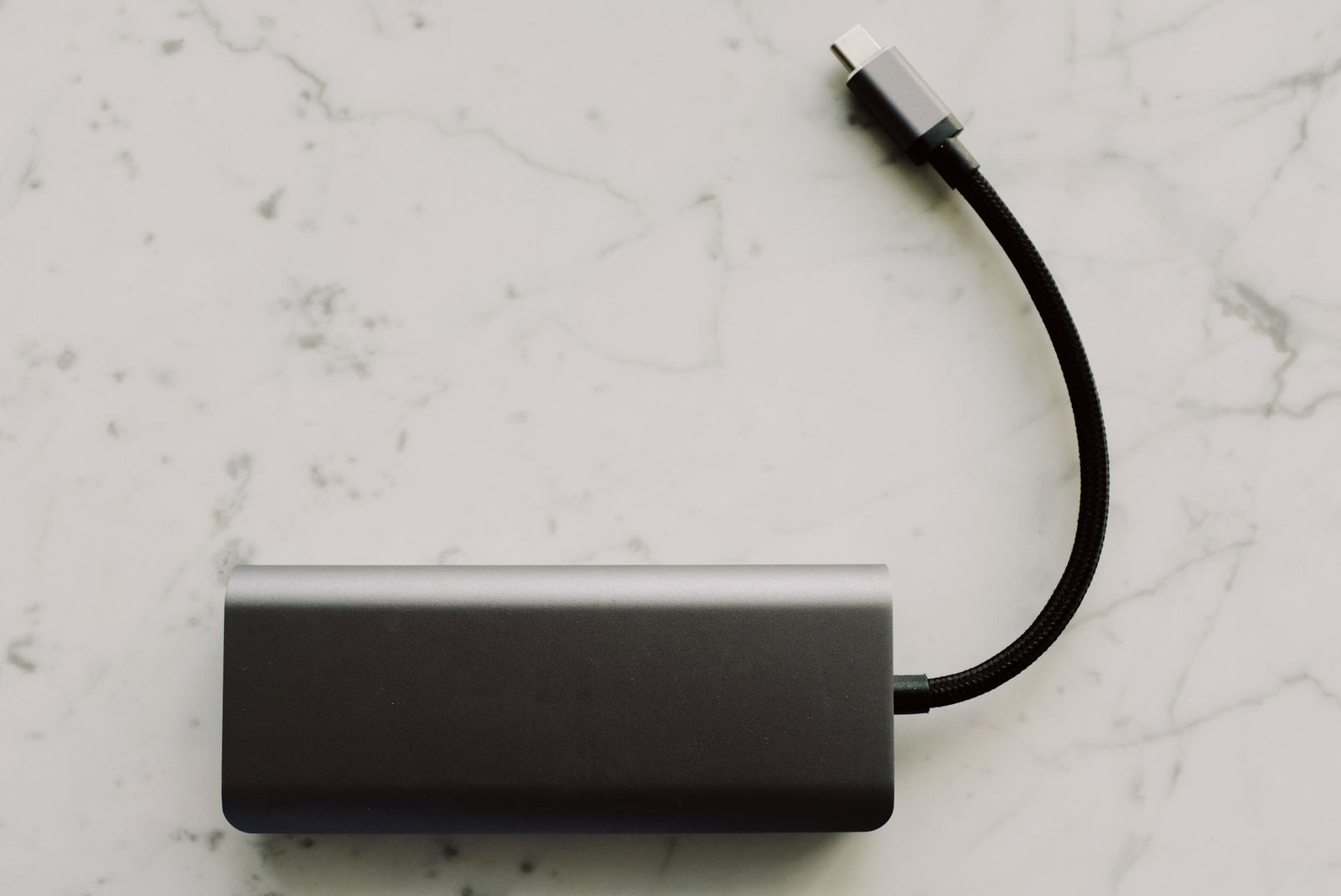 Grijs apparaatje met een gevlochten USB-C-kabel op een marmeren tafel