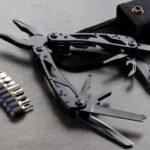 Zwarte multitool met uitgeklapte tang, zaag en mesjes naast een set bits