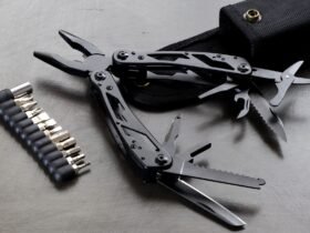 Zwarte multitool met uitgeklapte tang, zaag en mesjes naast een set bits