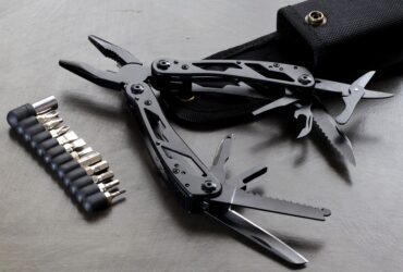 Zwarte multitool met uitgeklapte tang, zaag en mesjes naast een set bits