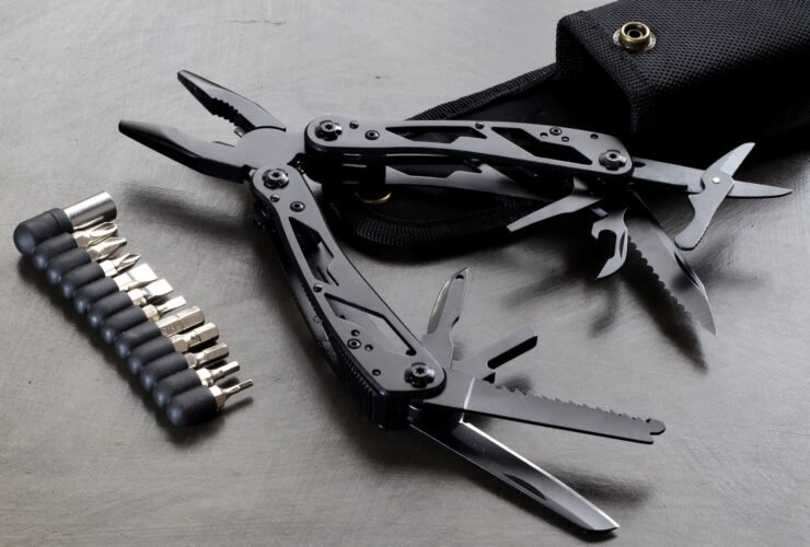 Zwarte multitool met uitgeklapte tang, zaag en mesjes naast een set bits