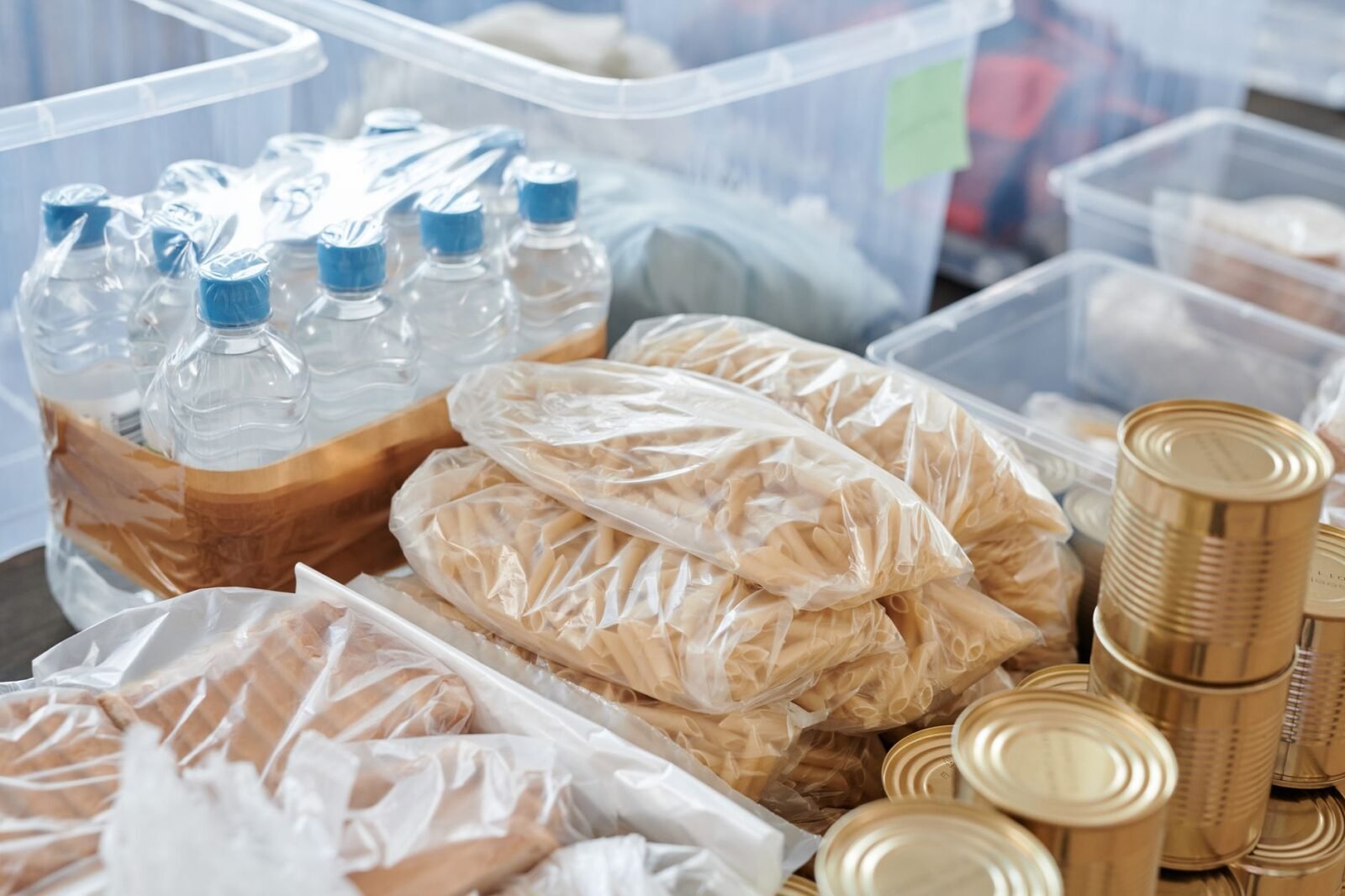 Voorraad flessen water, pasta en blikken voedsel in opbergbakken