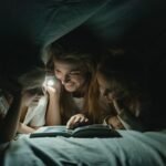 Moeder en kinderen onder een deken met een zaklamp tijdens een stroomstoring