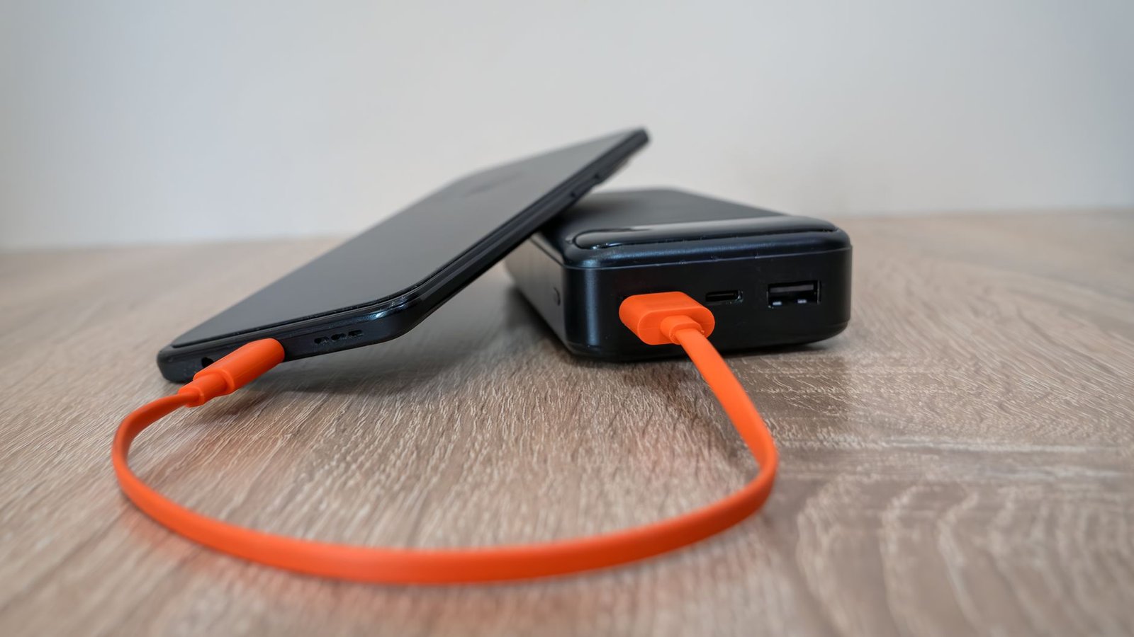 Telefoon wordt opgeladen met een powerbank via een oranje kabel