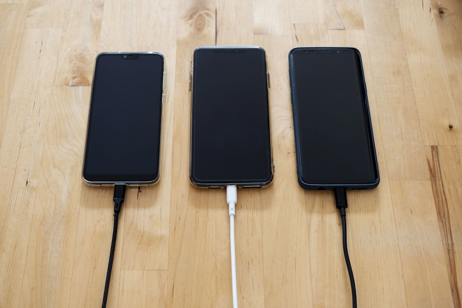 Drie telefoons liggen naast elkaar aan de oplader op een houten tafel